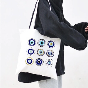 White canvas tote bag with turquoise Evil Eye patterns worn by a model in a minimalist style