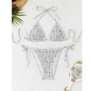 Flat lay of smocked lavender floral triangle bikini set with summer vacation accessories