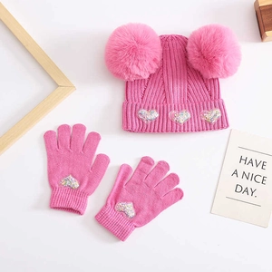 Detail of pink knitted baby hat and gloves set with pom-poms and sequined heart patches