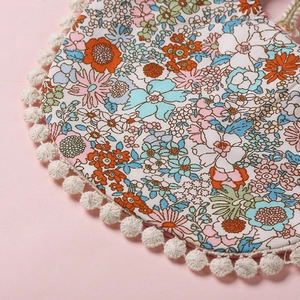 Détail d'un bavoir floral pour bébé avec bordure pompon et texture en coton doux