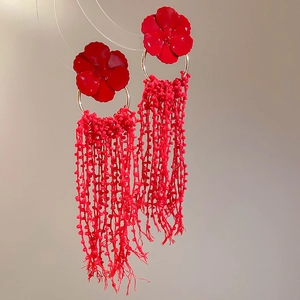 Close-up of vibrant red floral earrings with long beaded tassels and glossy petals