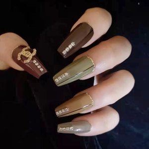 Dettaglio di unghie finte cachi e verde militare con logo in metallo e strass di lusso
