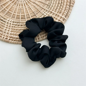 Detailed view of large black matte satin scrunchie with soft fabric pleats