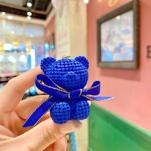 Close-up of a blue bear keychain with a woven texture and decorative satin bow