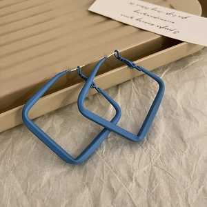 Macro detail of blue matte square geometric earrings on a minimalist cream tray