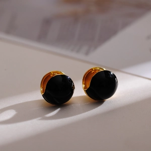 Macro detail of French vintage black enamel and gold plated ball hoop earrings on paper