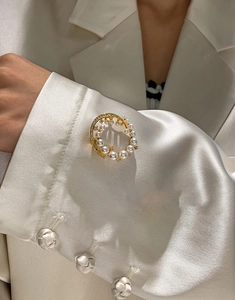 Detail of 24k gold-plated pearl brooch with sparkling crystals on white satin suit