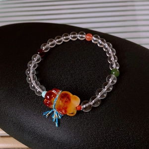 Detail of beaded bracelet with white crystal, amber beast charm and blue yellow tassels