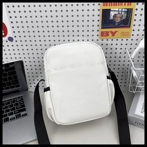 Minimalist white crossbody bag with adjustable black strap shown in a modern workspace