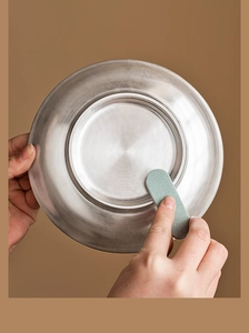 Close-up of cleaning a silver tea cup base with a green scouring pad on a brown background