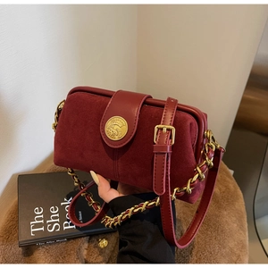 Close-up of burgundy suede doctor bag with vintage gold emblem and chain strap detail