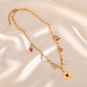 Gold chain necklace with strawberry, cherry, pearl, and heart pendants on silk fabric