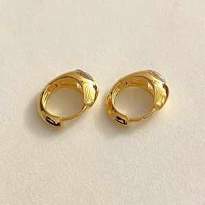 Detailed view of gold hoop earrings with clear zircon stones on textured background