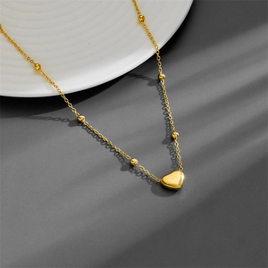 Elegant gold titanium heart necklace with Love engraving and beaded chain on a white plate