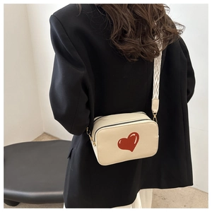 Detail view of cream crossbody bag featuring a red heart and textured wide strap