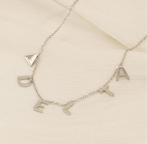 Détail du collier en titane argenté avec lettres DELTA sur tissu crème