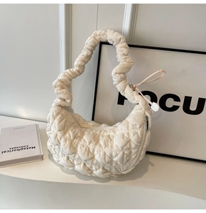 Detail of off-white quilted dumpling bag with scrunchie strap on white pedestal