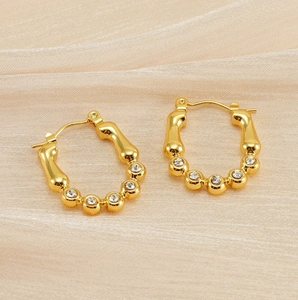 Gros plan détaillé des créoles dorées style bambou avec strass sur fond en soie beige