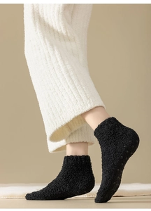 Close-up of black fuzzy coral fleece socks with anti-slip silicone dots on the sole