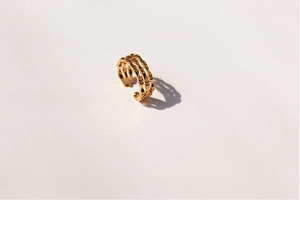 Macro shot of a golden triple-layer bamboo style open ring on a beige surface
