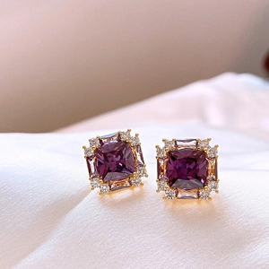 Close-up of vintage square earrings with purple gemstones and gold setting on soft fabric