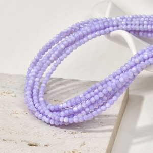 Close-up of 3mm purple natural shell beads layered on a beige stone and ceramic stand