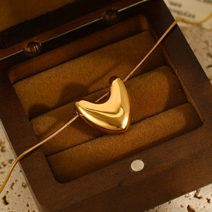 Close-up of a polished gold puff heart pendant on a snake chain inside a jewelry box