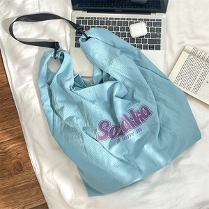 Détail du sac en toile à carreaux bleu clair avec lettrage violet sur lit blanc