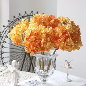 Detailed view of orange hydrangea faux flowers in a glass vase with retro decor items