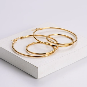 Set of two pairs of polished gold hoop earrings on a white stone display block