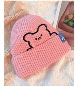 Detail of pink knitted beanie featuring black bear embroidery and a blue enjoy label