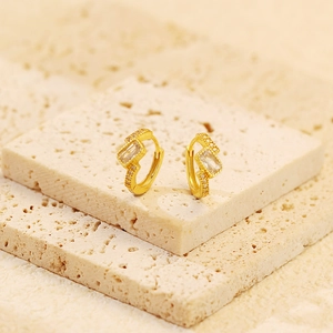 Macro shot of gold huggie earrings with clear cubic zirconia on natural stone slabs