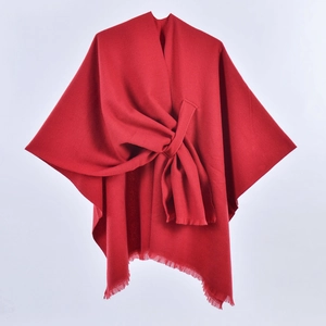 Detail of red knit poncho featuring a front knot design and stylish fringed hem tassels