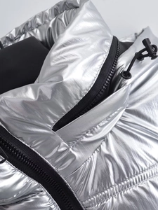Détail d'une doudoune argentée métallisée montrant le tissu brillant et le zip noir