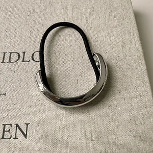 Detail of high-elastic black hair tie with polished silver curved metal geometric ornament