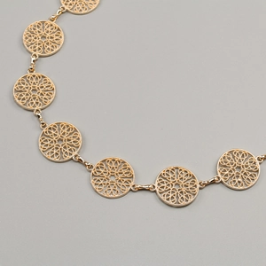 Detail of gold hollow circular links chain belt with intricate floral patterns on metal