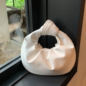 Minimalist white ruched handbag with a knotted handle shown in natural window light