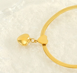 Detail of gold-plated snake chain necklace with double heart pendants on a textured base