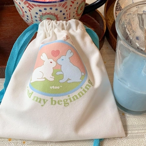 Close-up of a white canvas drawstring bag with cute rabbit print and light blue cords