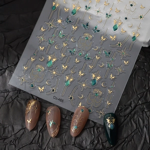 Detail of gold butterfly and star nail stickers shown on emerald and pink nails