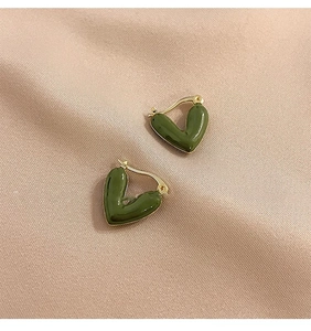 Detailed view of heart-shaped olive green enamel earrings with gold metal on pink silk