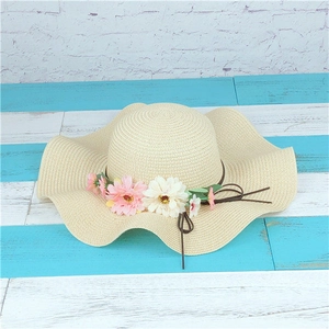 Close-up of beige woven straw hat featuring elegant wavy brim and floral decorations
