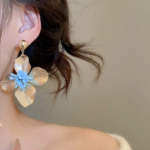 Macro detail of a golden flower earring with blue center petals on a female model