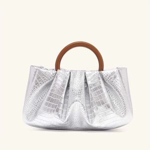 Detail of silver crocodile pattern clutch bag featuring a unique brown resin ring handle