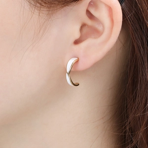 Close-up of a model wearing C-shaped gold stainless steel earrings with white enamel