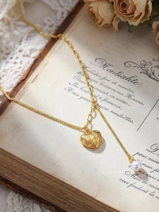 Détail du collier cœur doré avec perle blanche sur une page de livre romantique