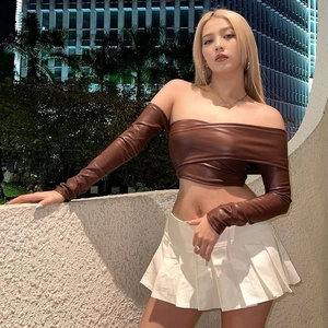 Dettaglio di crop top in ecopelle marrone con una minigonna a pieghe bianca
