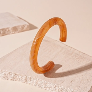 Detail of amber acrylic open bangle with marble texture on minimalist stone base