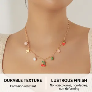 Detailed shot of a gold necklace featuring red cherries, strawberries, and pearl charms