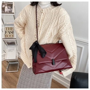 Détail du sac matelassé bordeaux avec nœud en soie noire et bandoulière chaîne